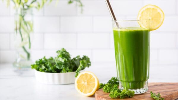 glass of green juice on a cutting board in a white kitchen with kale and lemons in the background