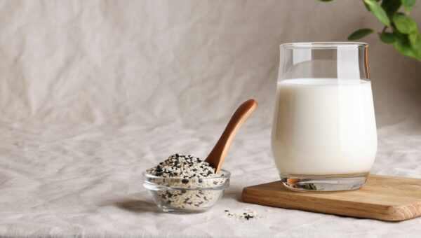 sesame seed milk in glass on textile background with plant