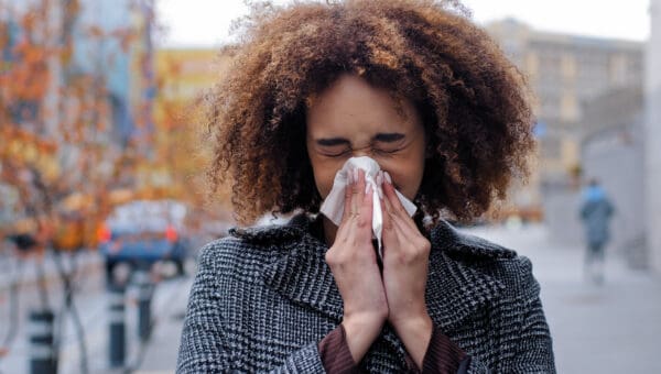 Woman sneezing on a street into a tissue