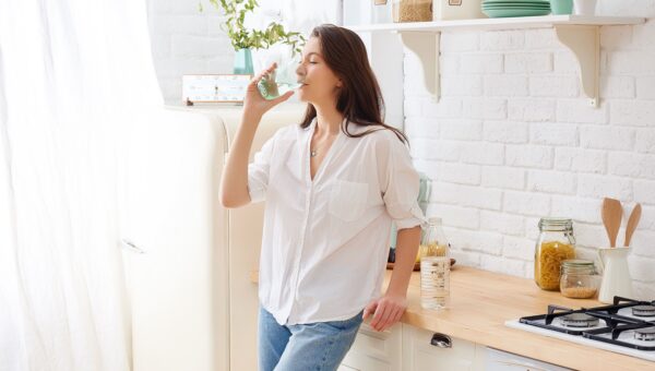 woman drinking water from a glass in a sunlit kitchen