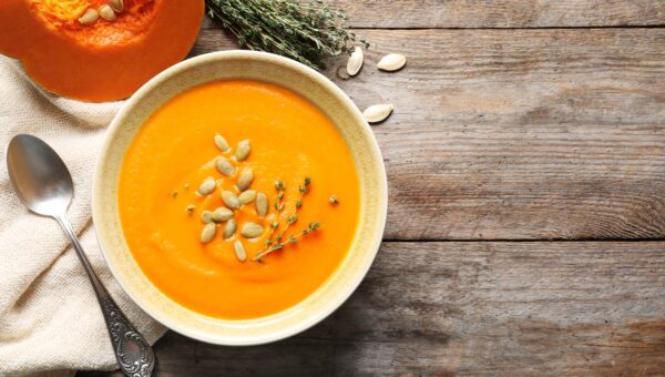 Flat lay composition with bowl of pumpkin soup on wooden background