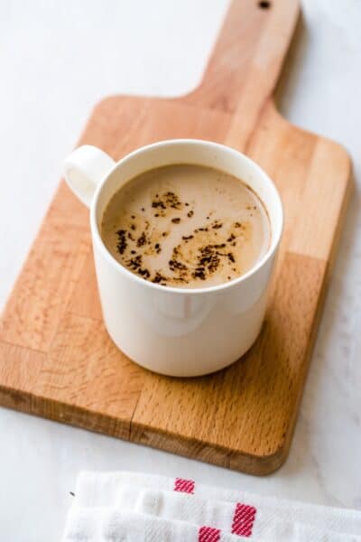 chaga latte with cinnamon sprinkled on top in a white mug on a wooden cutting board with white background