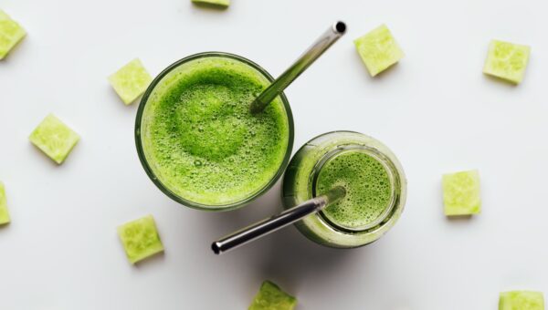 two glasses of cucumber juice on a white background with squares of cut out cucumber