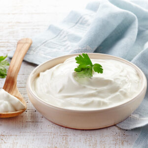 Thick white sauce in white dish with wooden spoon and blue towel in the background